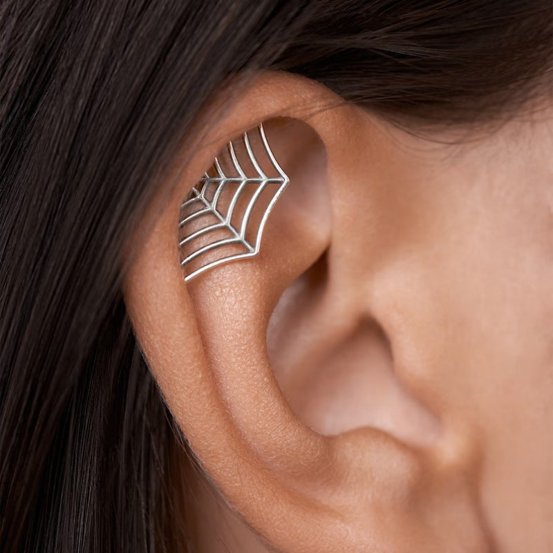 Silver spider web earring worn on a person's ear