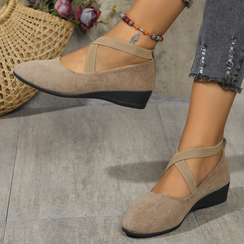 Beige suede shoes with black soles worn by a person on a gray floor.