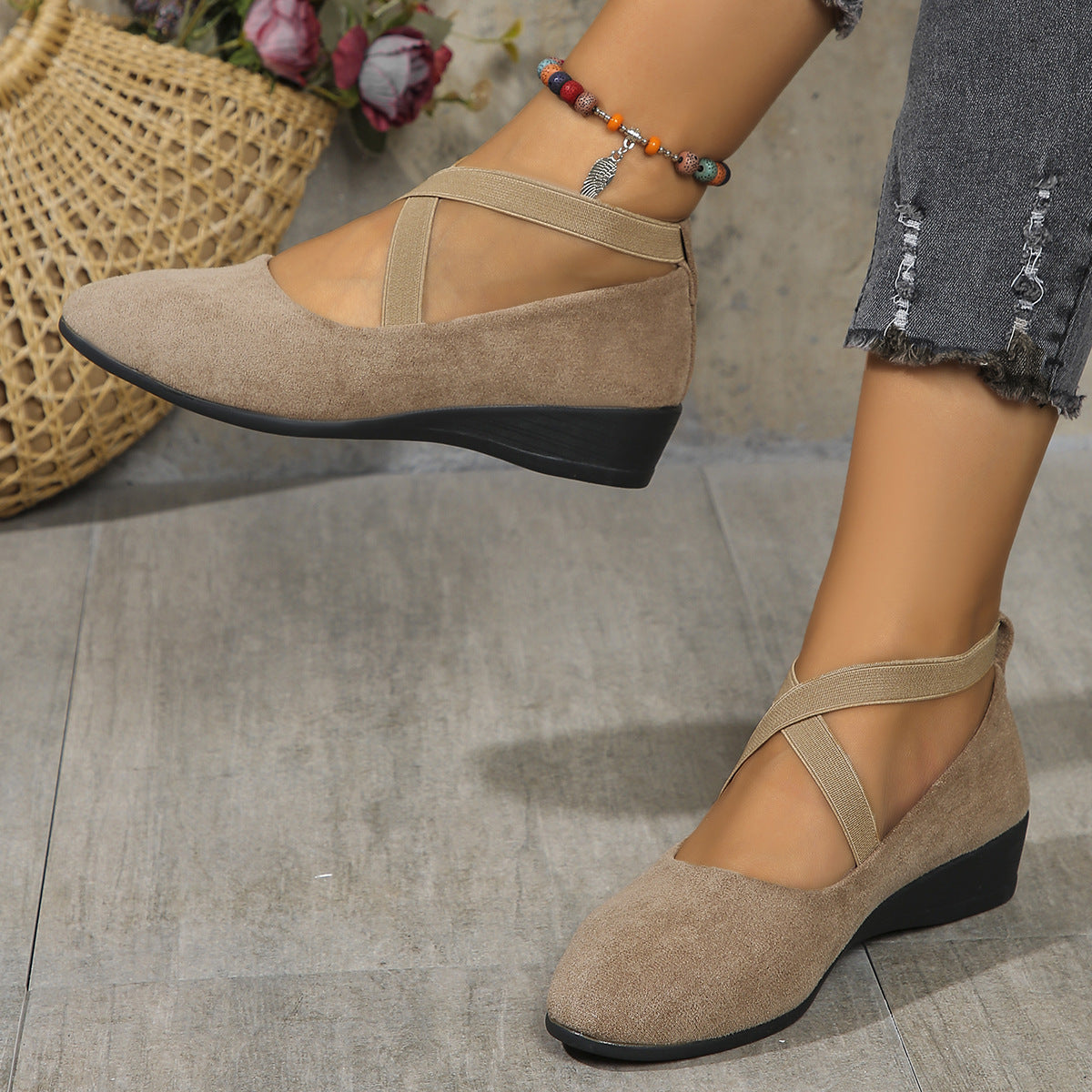 Beige suede shoes with black soles worn by a person on a gray floor.