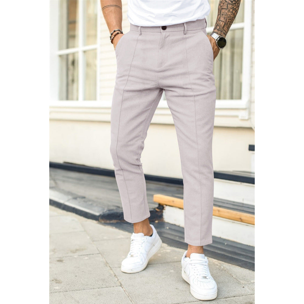 Person wearing light gray pants and white sneakers standing on a street.