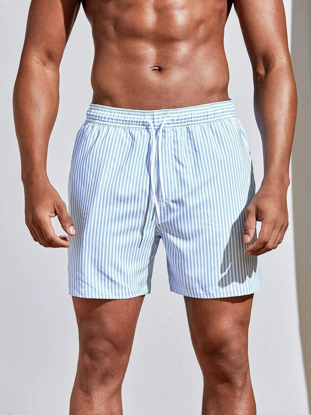 Man wearing light blue striped swim shorts on a plain background