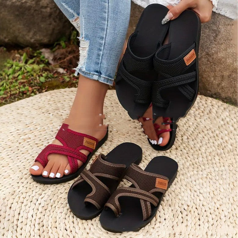 Black, red, and brown sandals on a textured surface with a blurred outdoor background.