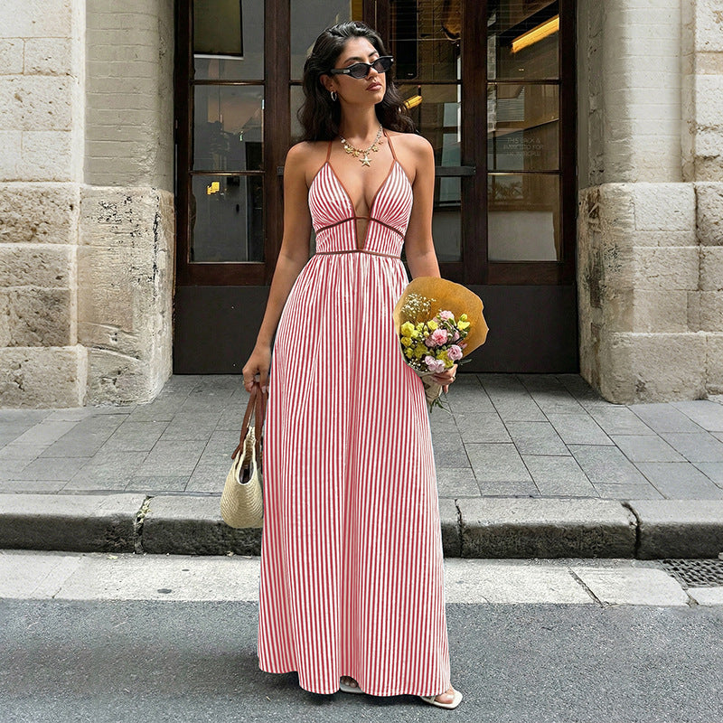 Woman in a pink striped dress holding flowers and a handbag on a city street.