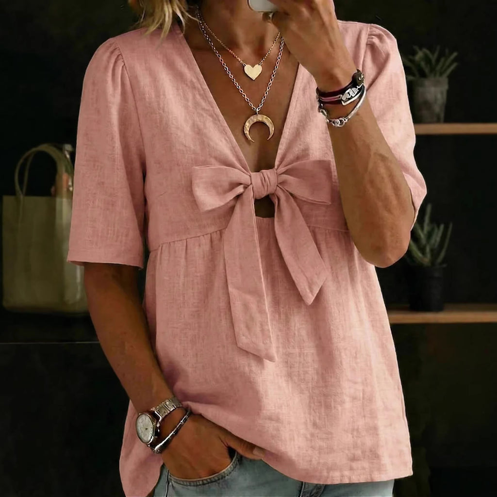 Person wearing a pink blouse with a bow detail, holding a phone.