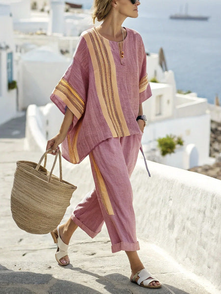 Woman in a pink outfit with yellow stripes walking on a sunlit street with white buildings in the background.