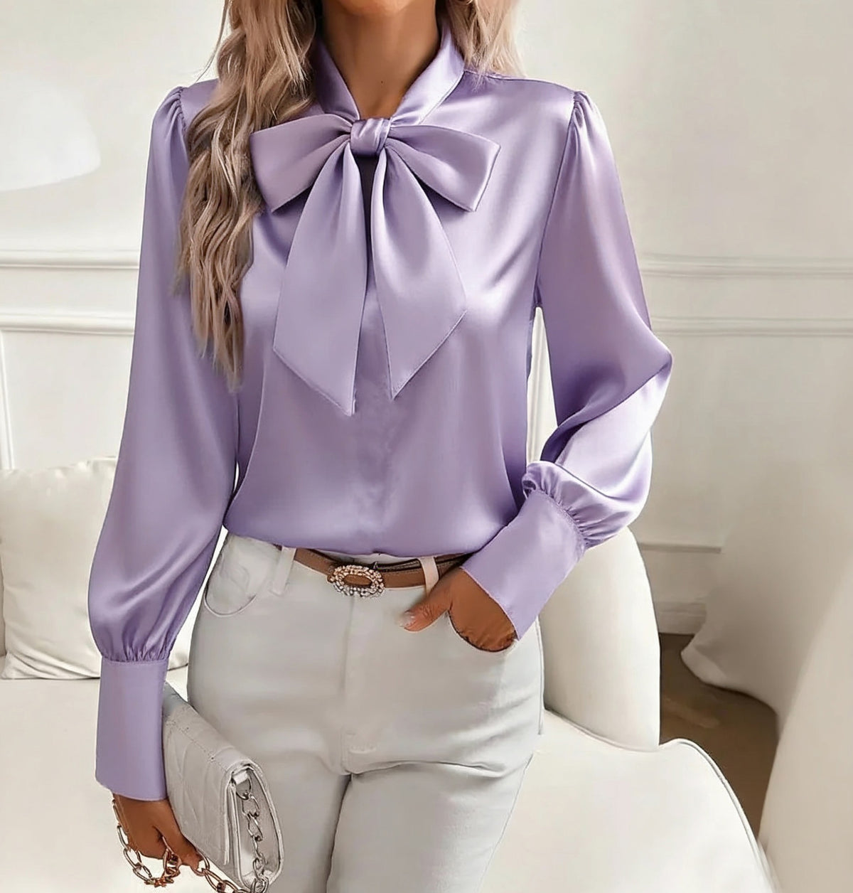 Person wearing a lavender blouse with a large bow tie and light-colored pants.