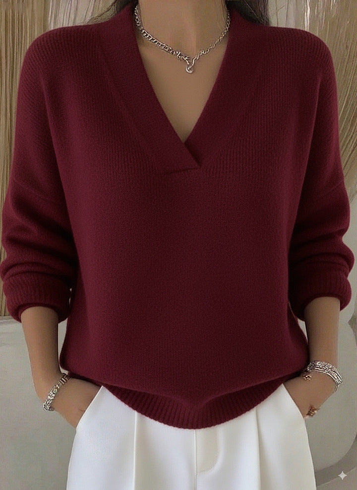 Person wearing a burgundy sweater and white pants with a neutral background
