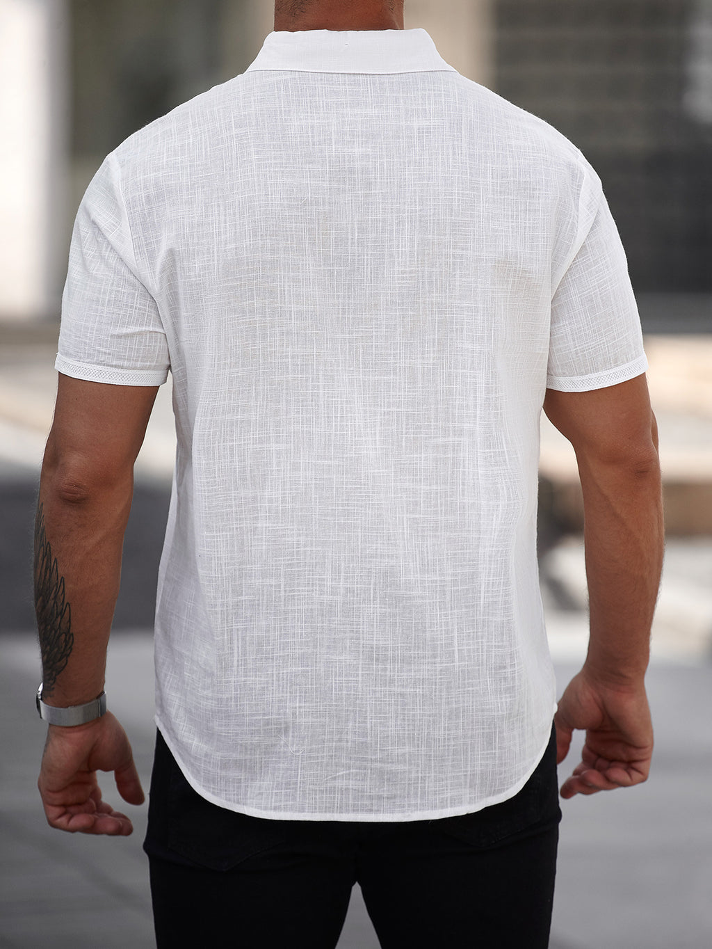 Person wearing a white short-sleeve shirt with a subtle pattern, standing outdoors.