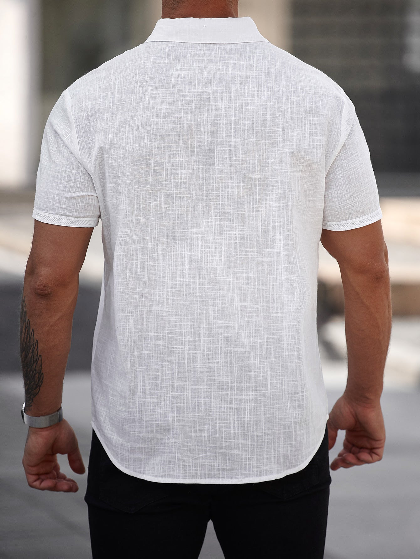 Person wearing a white short-sleeve shirt with a subtle pattern, standing outdoors.