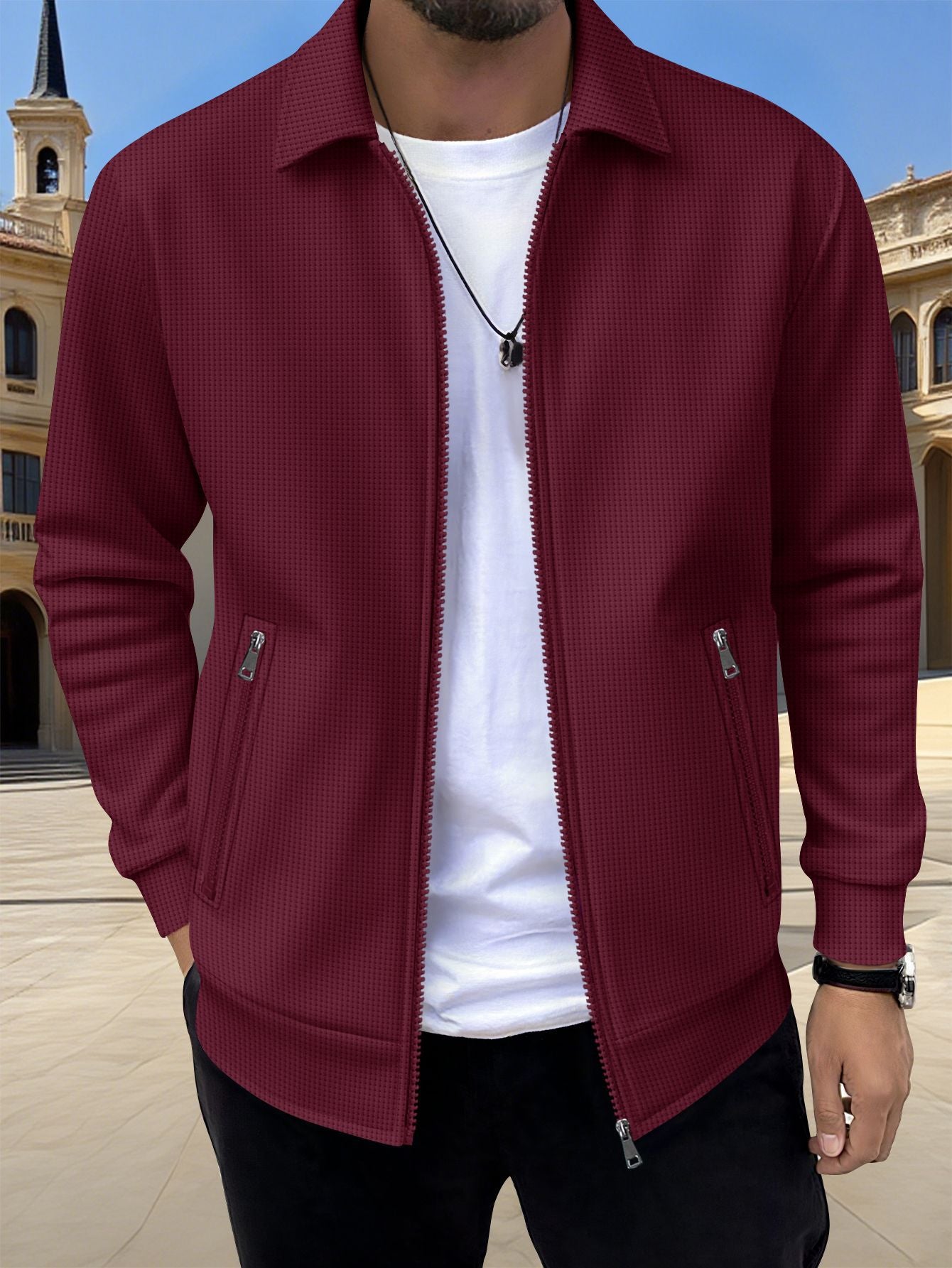 Person wearing a burgundy jacket over a white shirt with a blurred architectural background