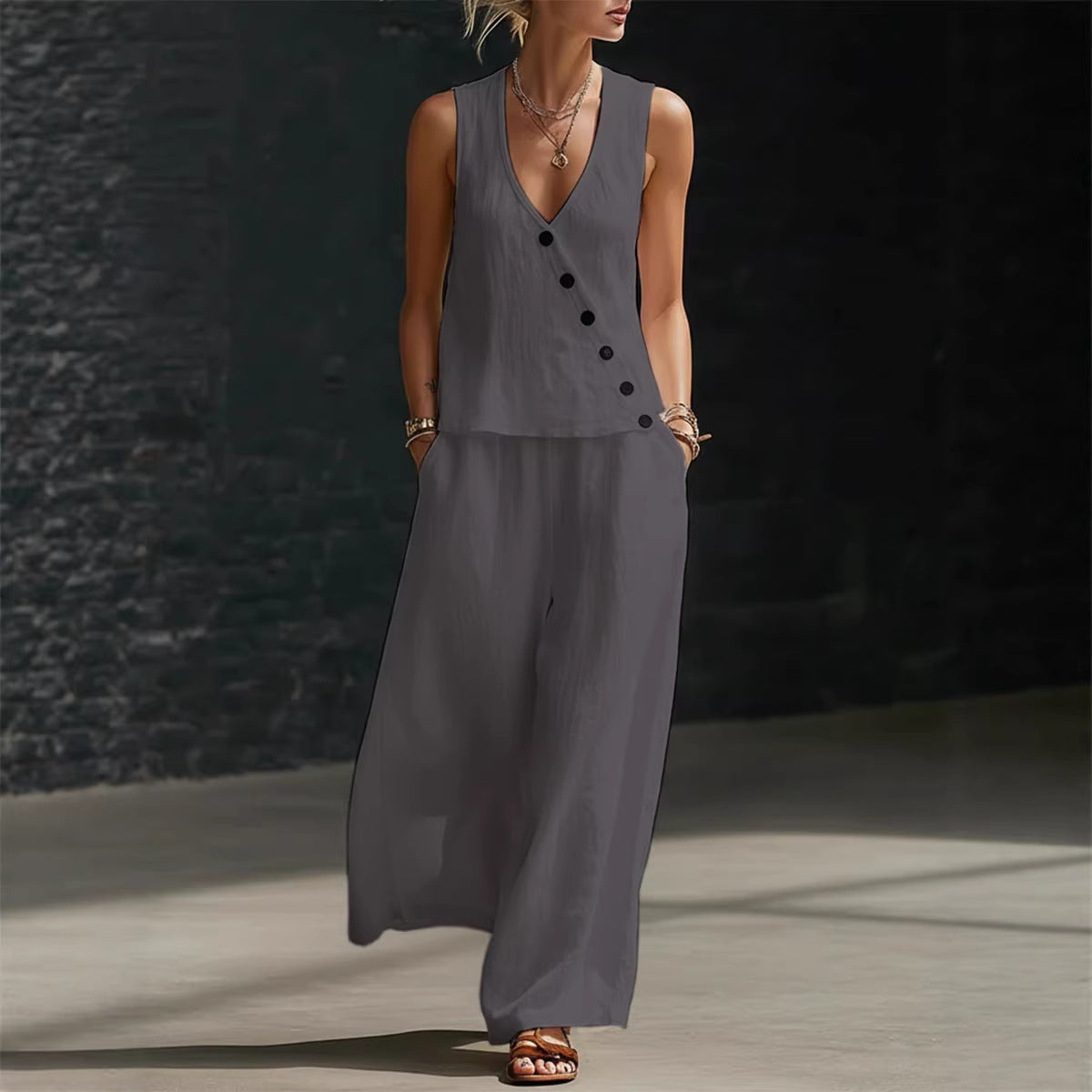 Woman wearing a long gray sleeveless dress against a dark textured wall.