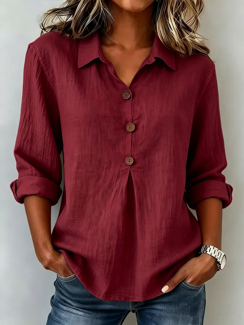Person wearing a burgundy button-up shirt with rolled-up sleeves against a plain background