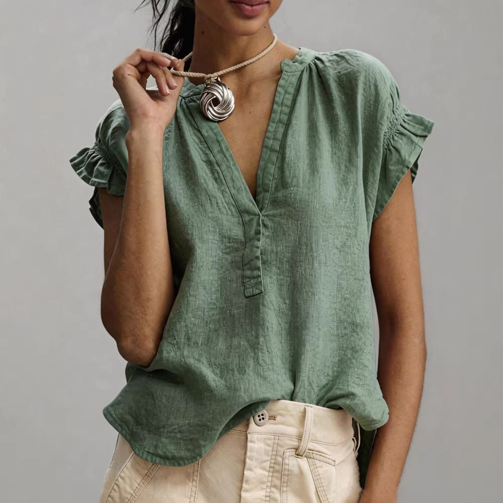 Woman wearing a green blouse with ruffled sleeves against a gray background