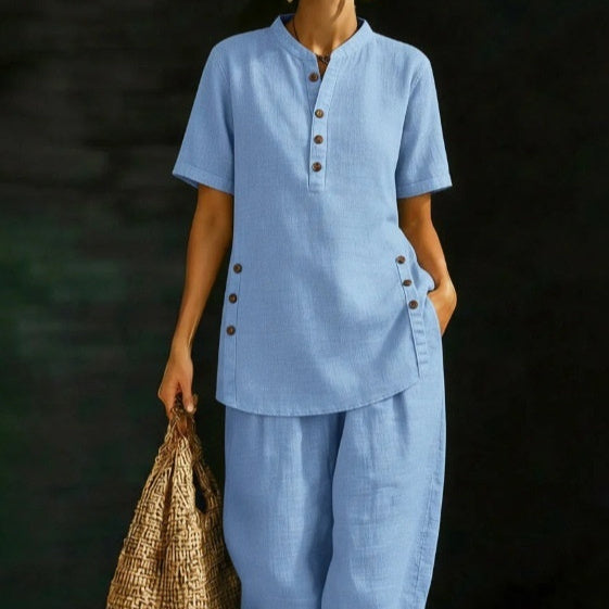 Person wearing a blue outfit with buttons, holding a woven bag against a dark background