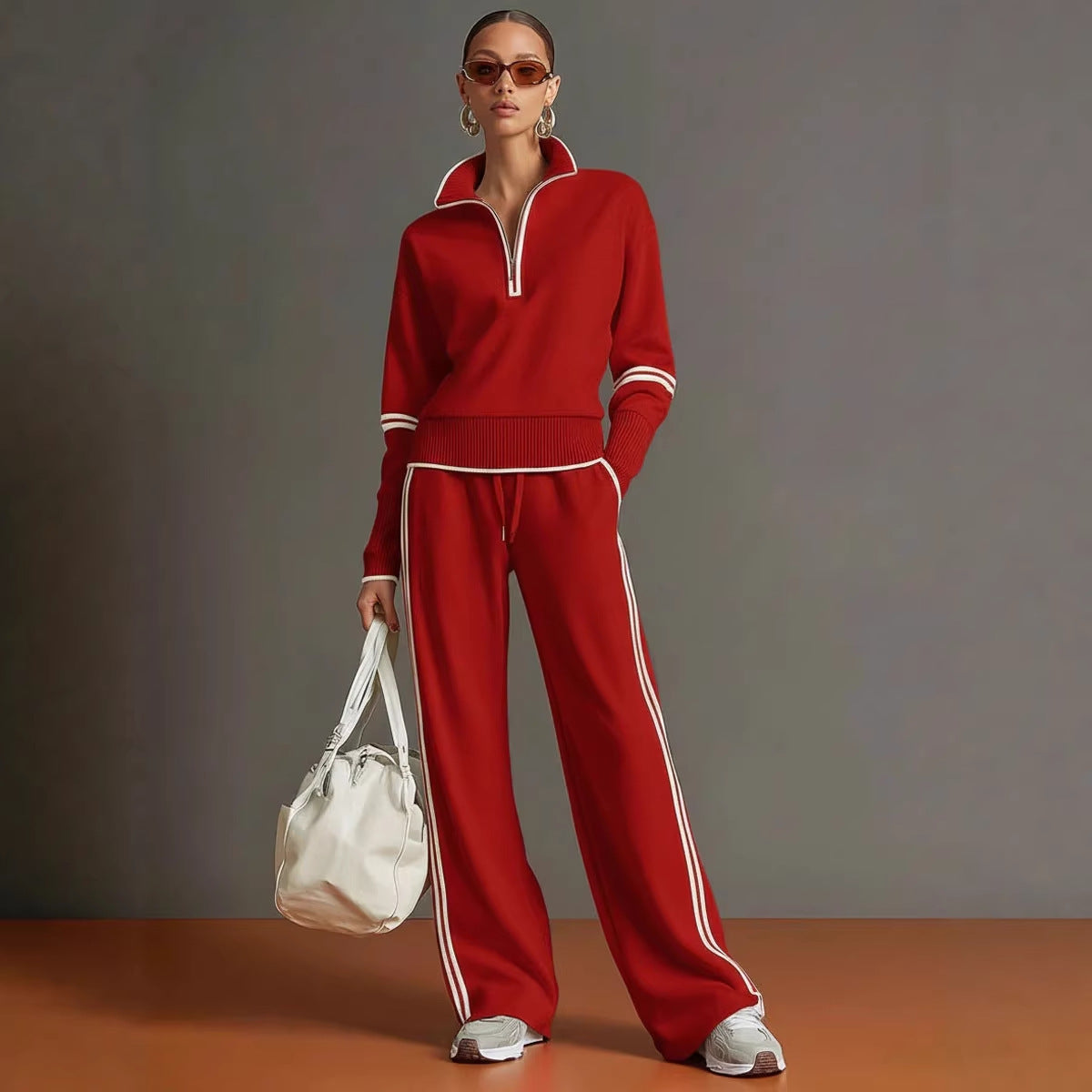 Woman wearing a red tracksuit with white stripes, holding a white bag against a gray background.