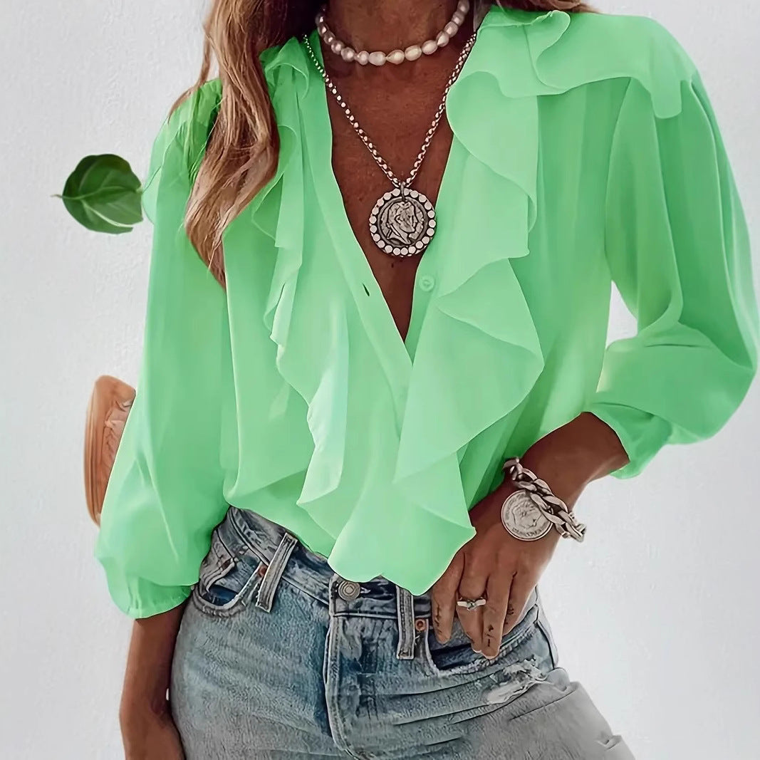 Person wearing a green blouse with ruffled details, denim jeans, and layered necklaces on a white background.