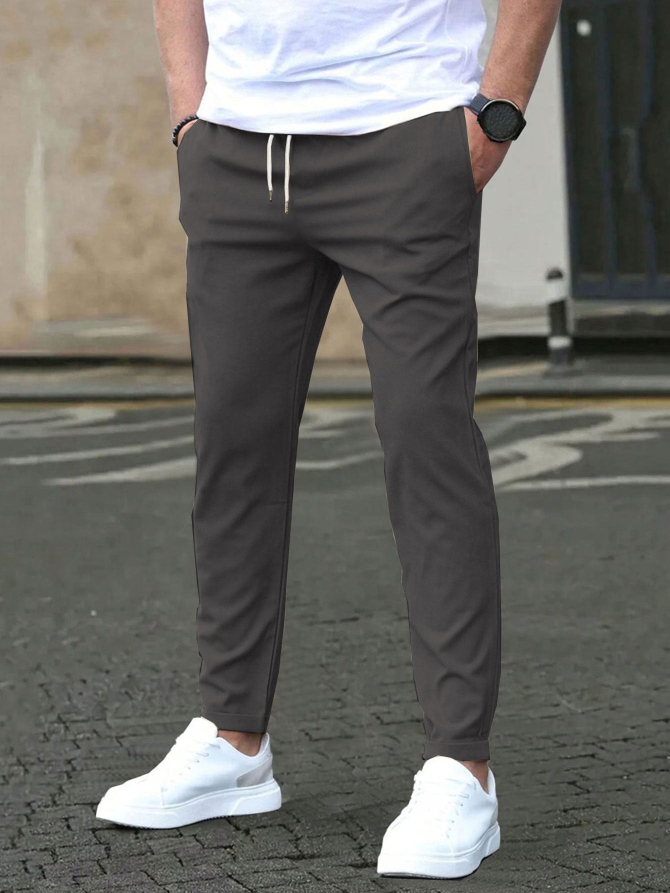 Person wearing gray jogger pants and white sneakers on a street.
