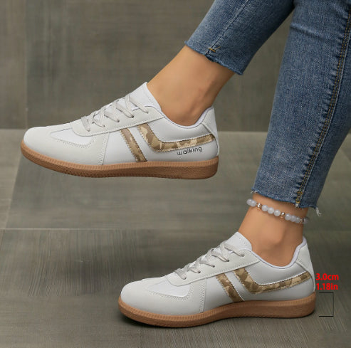 White sneakers with brown soles worn by a person on a gray surface