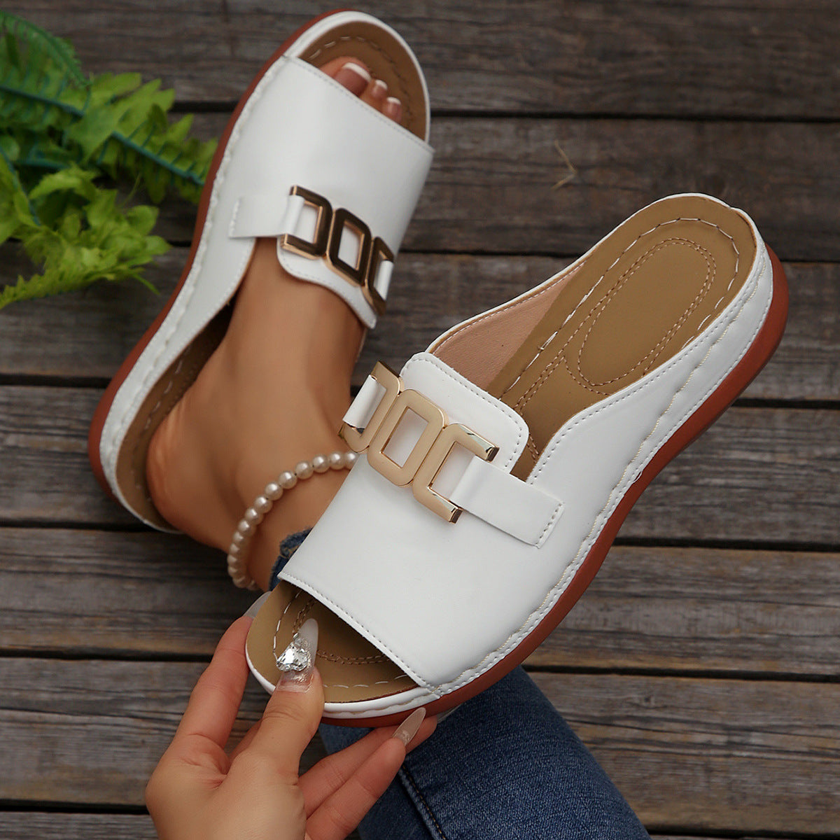 White sandals with gold buckles on a wooden surface
