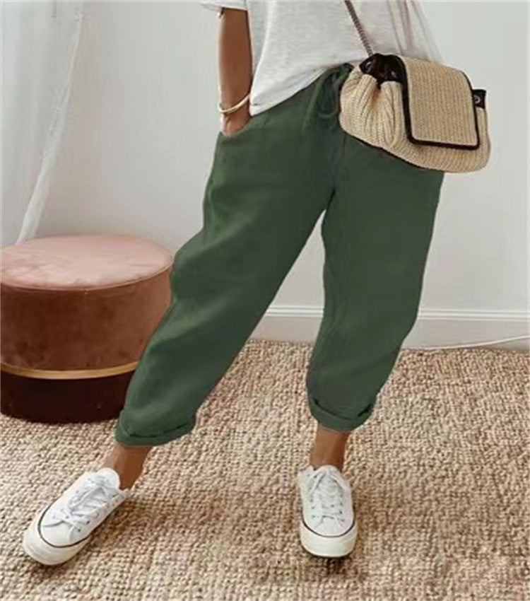 Person wearing green pants and white sneakers with a beige bag, standing on a carpeted floor.