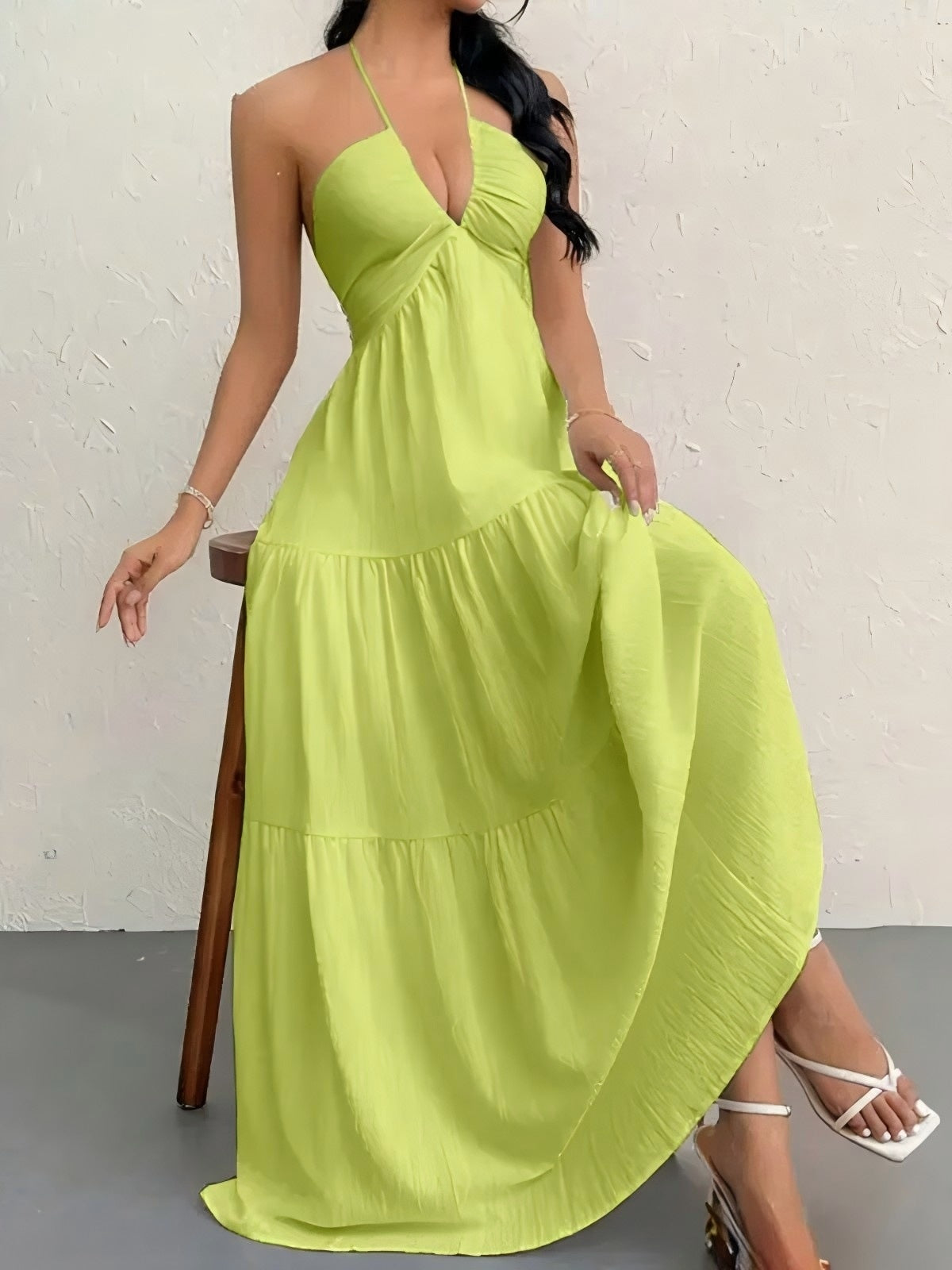 Woman wearing a bright green dress sitting on a stool against a white wall.