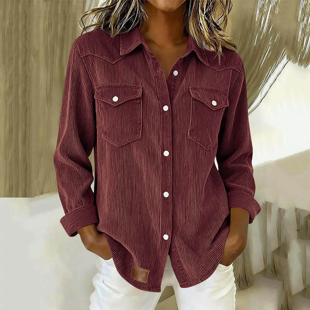 A woman wearing a long-sleeve corduroy button-up shirt in a deep burgundy color, paired with white pants, shown in a styled indoor setting.