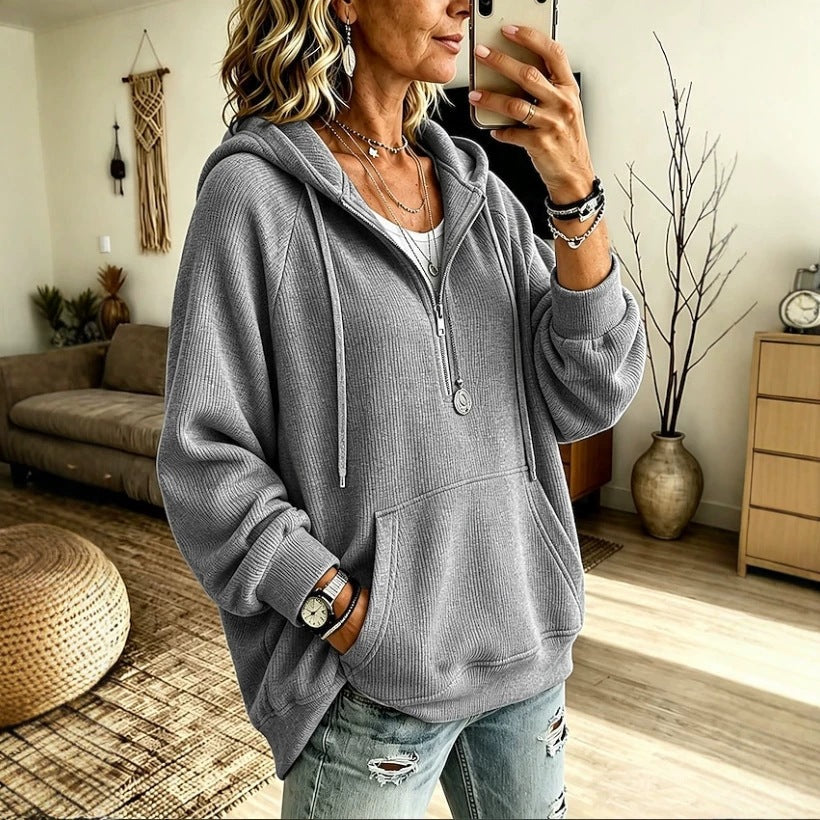 A woman takes a mirror selfie in a cozy living room while wearing a gray waffle-knit zip-up hoodie with a front kangaroo pocket and distressed light-wash jeans.