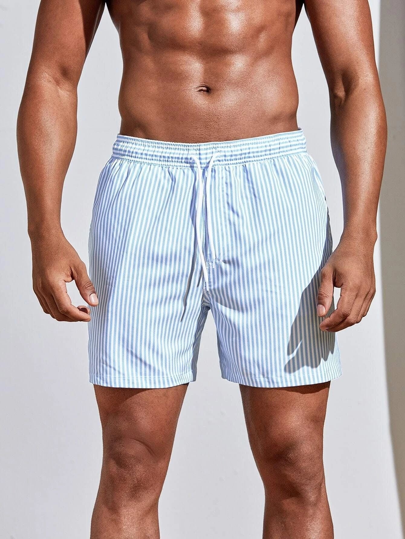Man wearing light blue striped swim shorts on a plain background