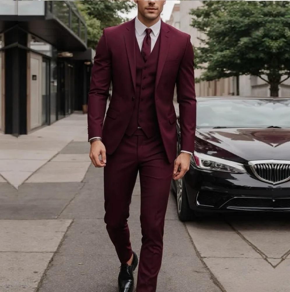 Man in a burgundy suit walking on a sidewalk with a car in the background