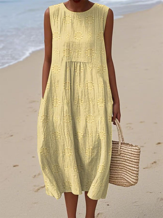 Woman in a yellow dress standing on a beach with a woven bag.