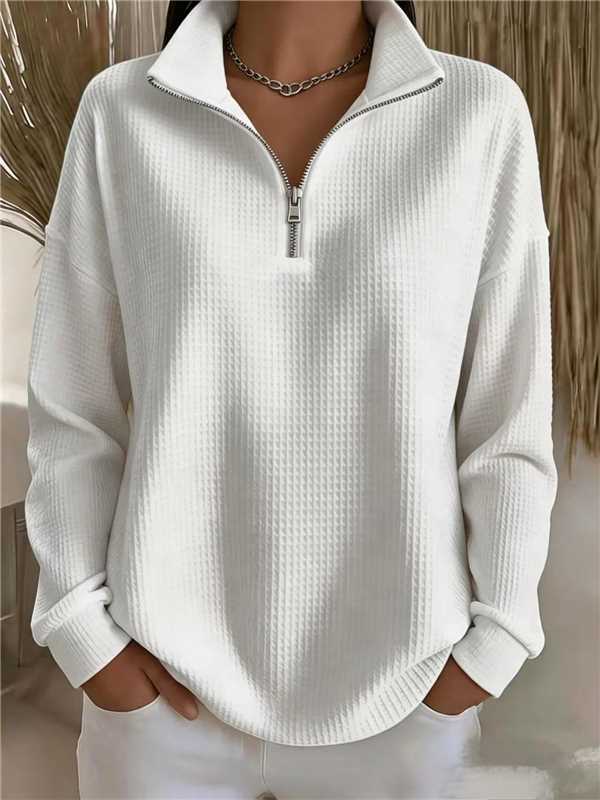 A person wearing a white waffle-knit long-sleeve quarter-zip pullover sweater with a stand collar, shown from the neck down against a softly blurred indoor background.