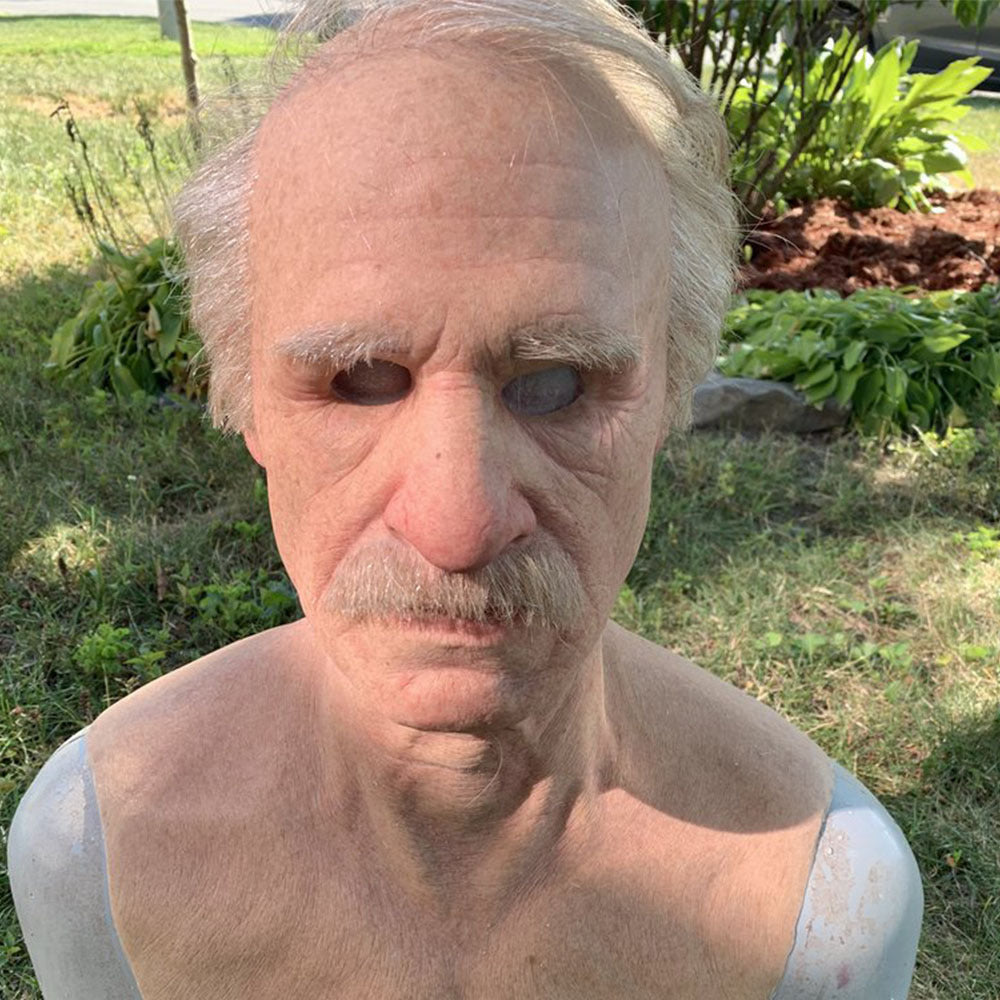 Man with a mustache and no shirt standing outdoors in a garden