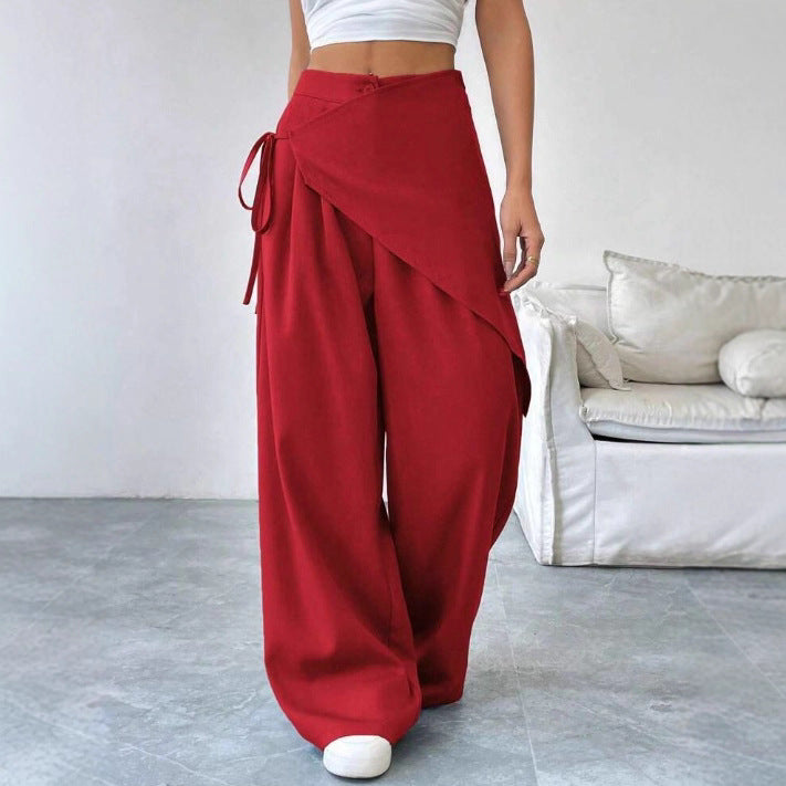 Person wearing red wide-leg pants and a white top in a minimalistic room.