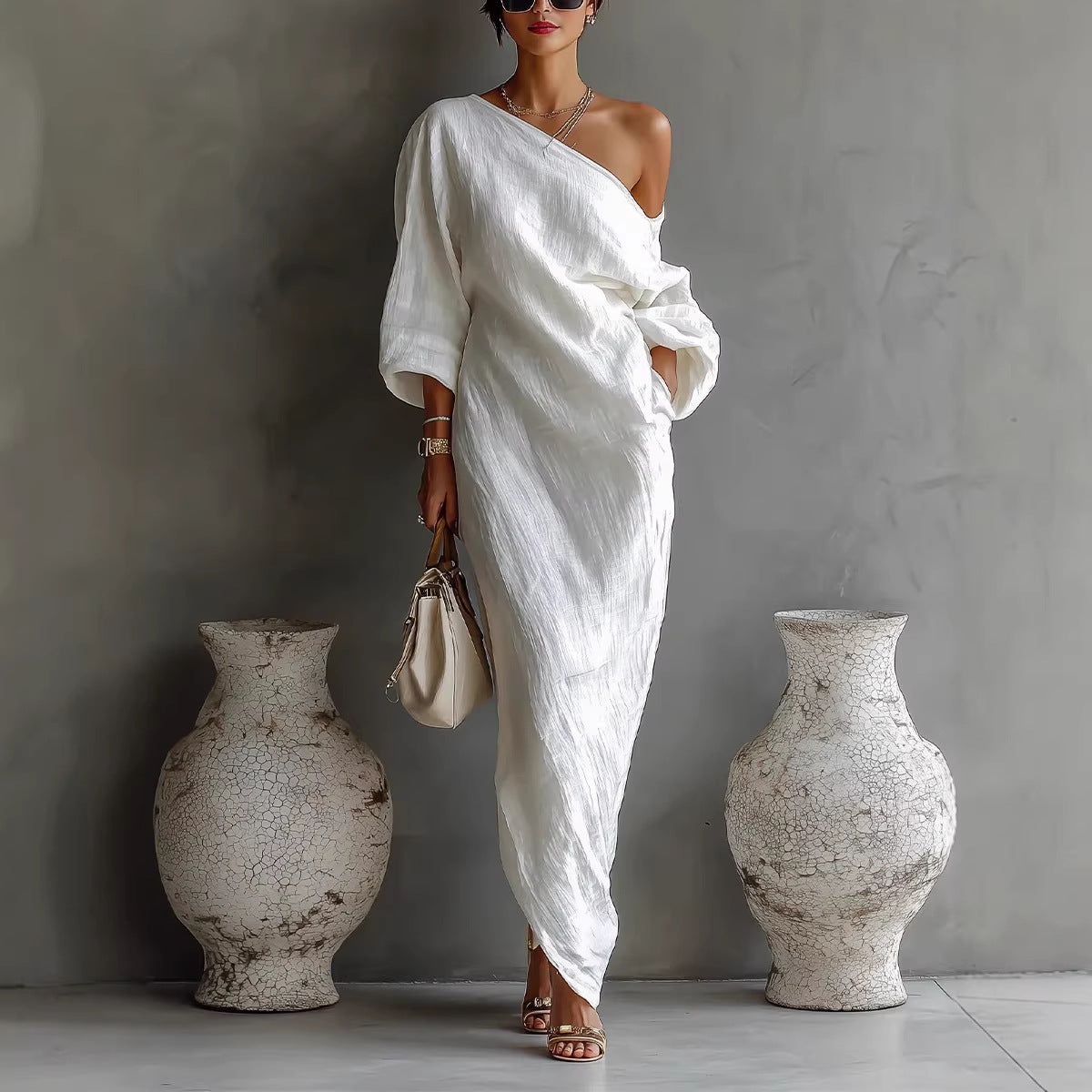 Woman in a white one-shoulder dress standing between two large vases against a gray wall.