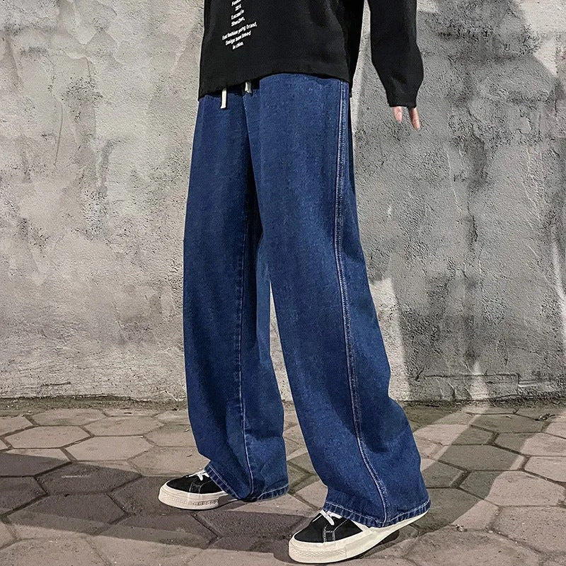 Person wearing blue jeans and black shoes standing against a textured wall.
