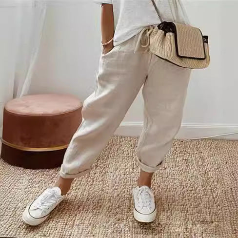 Person wearing beige jogger pants, white sneakers, and a straw bag indoors.