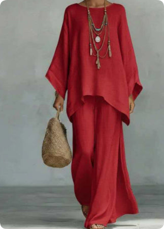Person wearing a red outfit with wide sleeves and long pants, holding a woven bag against a plain background.