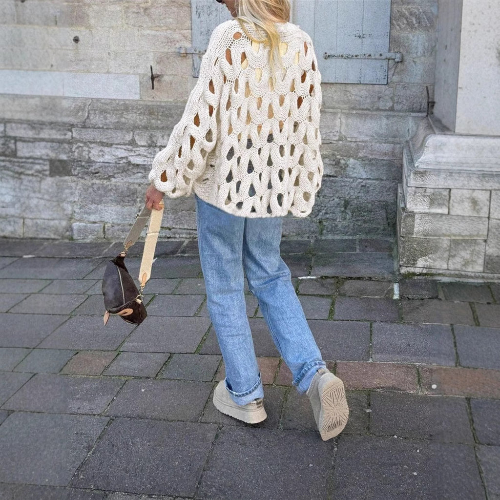 Person wearing a white textured sweater and blue jeans walking on a stone pavement.