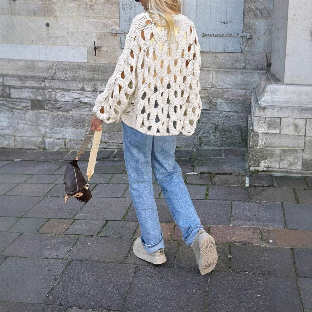 Person wearing a white textured sweater and blue jeans walking on a stone pavement.