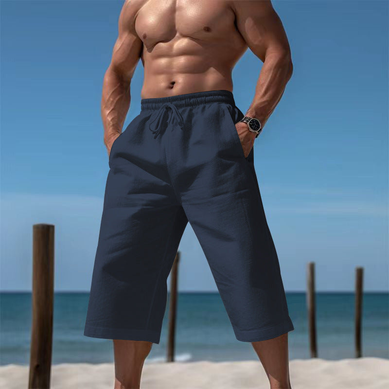 Man wearing navy blue shorts on a beach with clear blue sky and ocean.