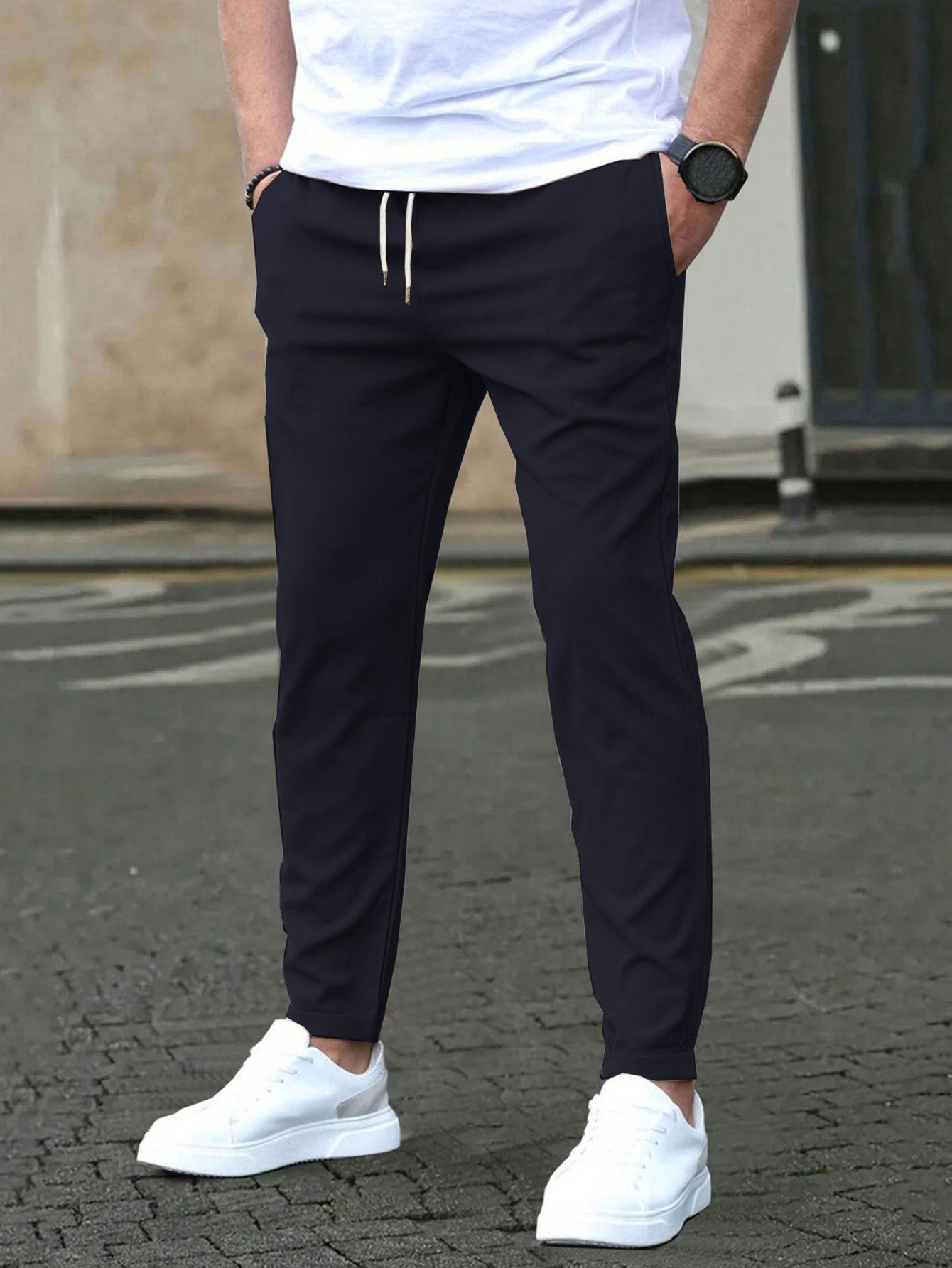 Person wearing navy jogger pants and white sneakers on a street.