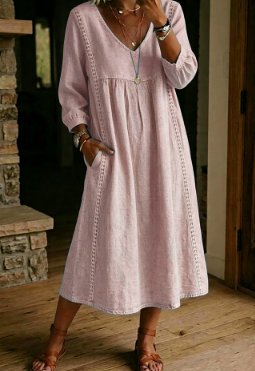 A woman wearing a light pink linen-blend midi dress with three-quarter sleeves, a V-neckline, and side pockets, standing in a rustic indoor setting with wooden floors and a stone wall.