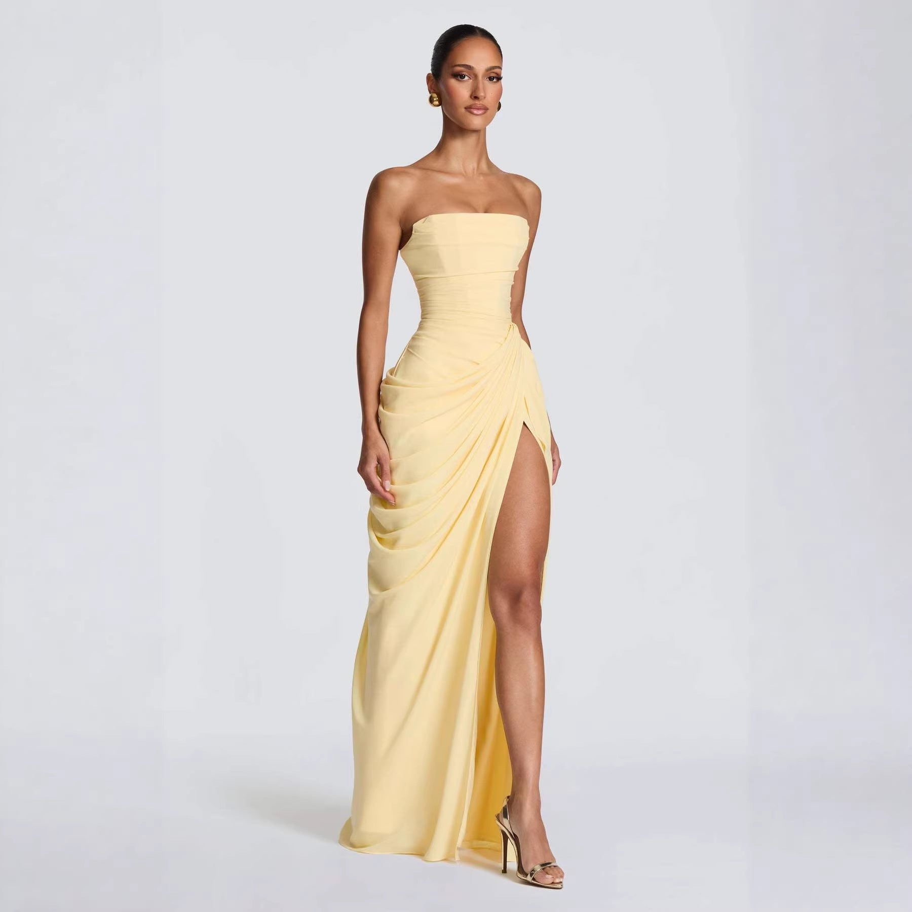 Woman wearing a strapless yellow evening gown with a slit on a white background