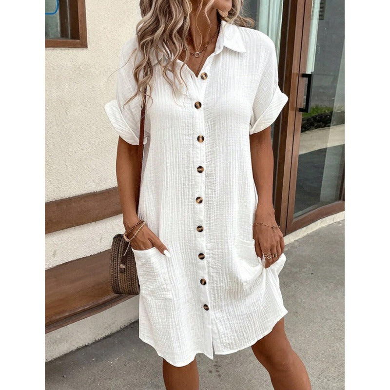 Woman wearing a white button-up dress standing outdoors.
