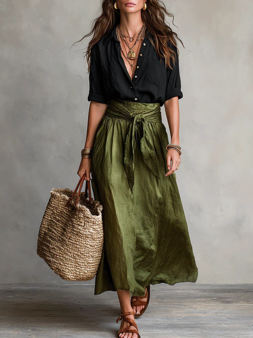 Woman wearing a black shirt and green skirt holding a woven bag against a neutral background