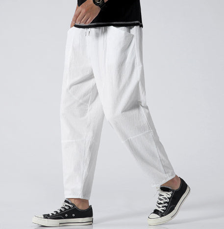 Person wearing white pants and black sneakers on a plain background