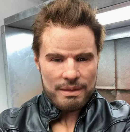 A close-up selfie of a man with styled brown hair and a short beard, wearing a black leather jacket in front of a metallic industrial background.