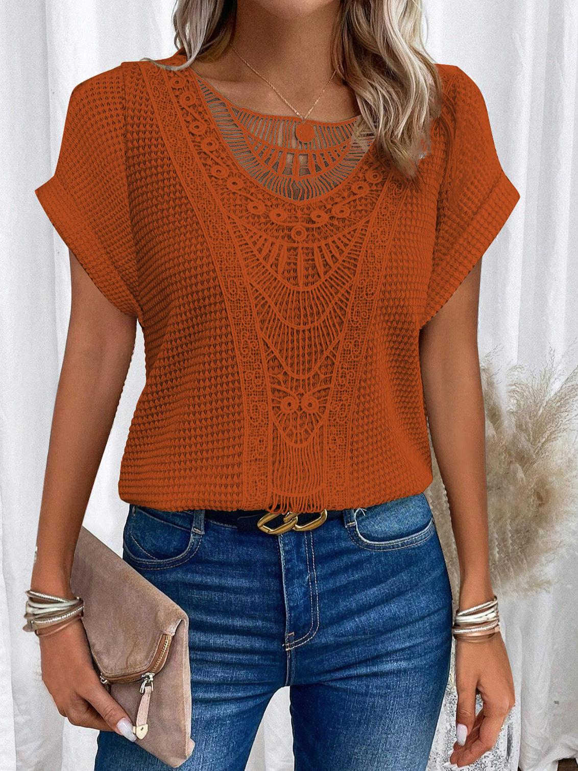 Person wearing an orange crochet top and blue jeans with a white curtain background