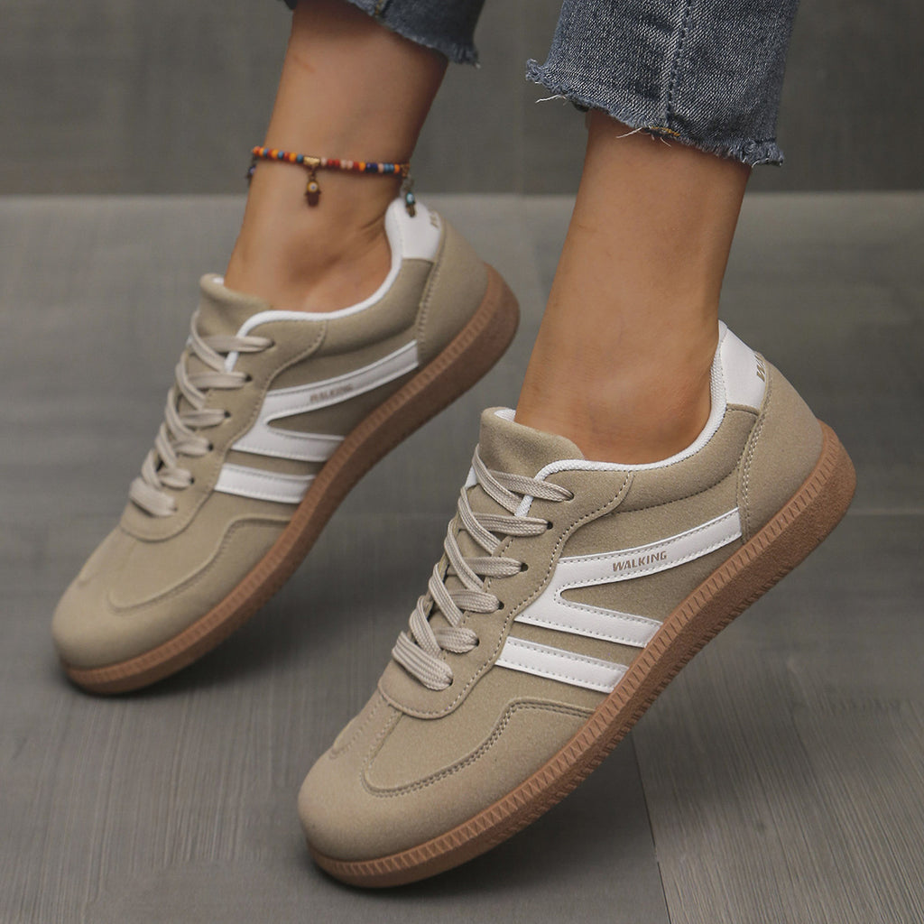 Beige sneakers with white stripes worn by a person on a gray floor.