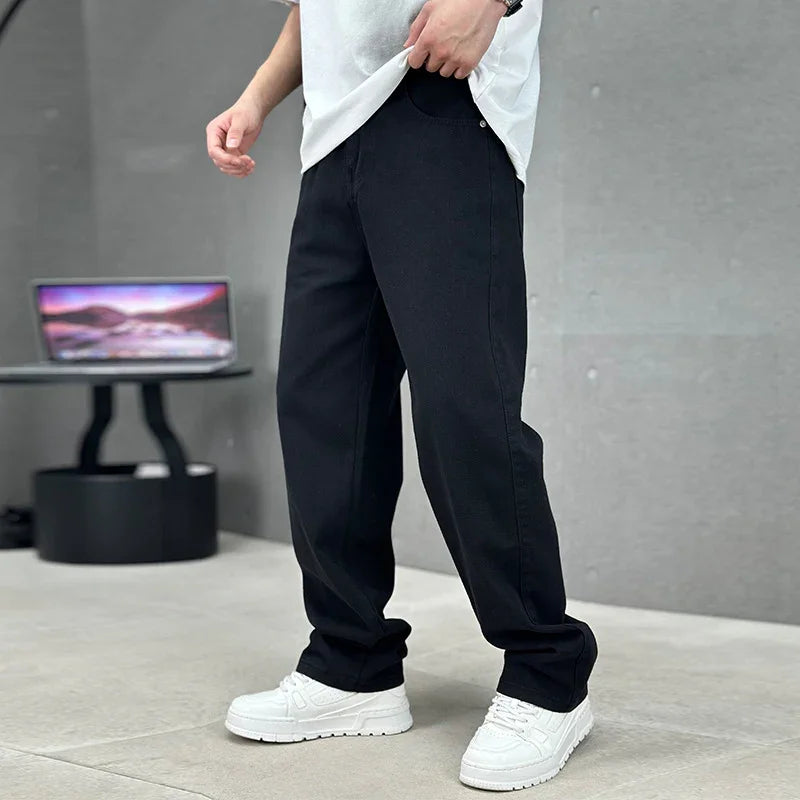 Person wearing black pants and white sneakers in a minimalistic setting with a laptop in the background.